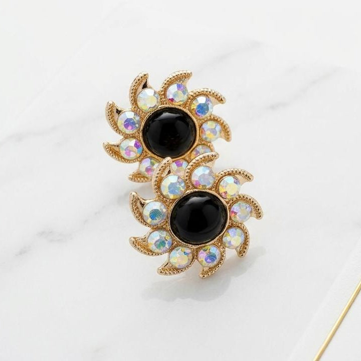 Decorative earrings with black gemstones on a white surface with 'Auree' branding.